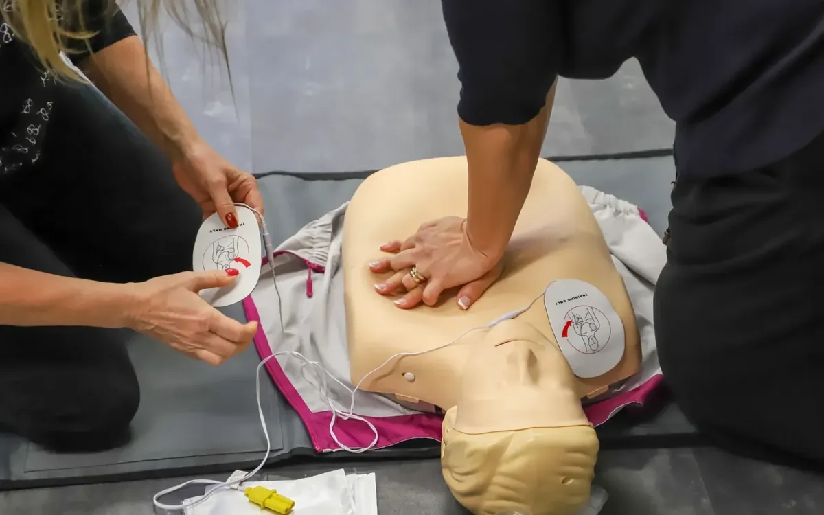 Team practicing CPR with AED pads: group booking first aid for workplaces